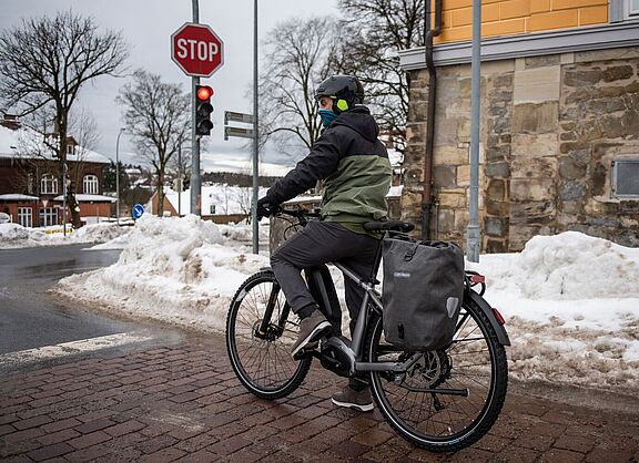 Im Winter an der Ampel. Ein Mann steht mit Fahrrad an einer Ampel in winterlicher Stadtlandschaft.